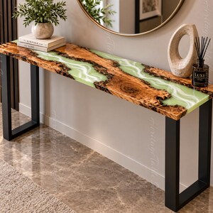 Puede incluir: Una mesa consola rectangular con un borde de madera natural y un río central de resina verde claro translúcida con patrones blancos en espiral. La mesa está sostenida por dos patas de metal negro en forma de U y tiene un acabado pulido.