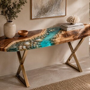 Può includere: Un tavolo console con un piano in legno a bordo naturale e un inserto centrale in resina blu che simula un fiume, decorato con ciottoli lisci e conchiglie. Il tavolo è sostenuto da due gambe in metallo dorato a forma di X.