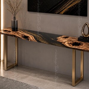 Può includere: Un tavolo console lungo caratterizzato da un piano in legno naturale con bordi irregolari, nodi e venature evidenti, integrato con una sezione centrale in resina nera liscia. Il tavolo è sostenuto da due gambe rettangolari in metallo oro spazzolato.