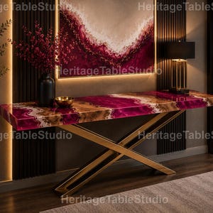 May include: A rectangular console table featuring a polished surface with a vibrant magenta and brown agate-inspired pattern, supported by a gold-toned metal base with intersecting X-shaped legs. A black vase with red flowers sits on the table.