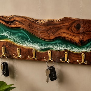 May include: A rectangular wall-mounted key holder made from a dark brown wood slab with a live edge. A central band of translucent emerald green resin features white wave-like patterns. Six gold-toned metal double hooks are attached to the wood.