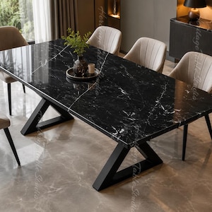 Op de afbeelding: Een rechthoekige eettafel met een gepolijst zwart marmeren blad met witte aders en een zwart metalen X-vormig onderstel. De tafel is omringd door zes gestoffeerde beige stoelen met verticale stiksels op de rugleuningen en donkere poten.