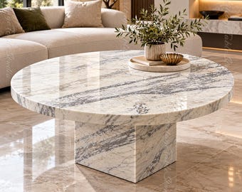 May include: A round coffee table featuring a polished white marble surface with prominent grey veining. The table is supported by a thick, square-shaped pedestal base made of the same matching marble material, creating a cohesive and solid structure.