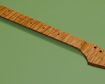 May include: A guitar neck crafted from light brown wood with a distinct tiger stripe grain pattern. The neck features a long fretboard with pre-drilled holes for frets and a headstock with six pre-drilled holes for tuning pegs at the end.