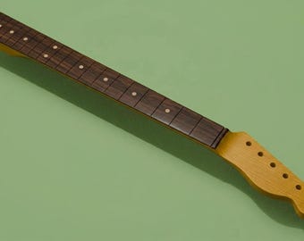 May include: A guitar neck featuring a dark brown wood fretboard with light-colored circular position markers and a light tan wooden headstock with six pre-drilled tuning peg holes arranged in a single line along the side.