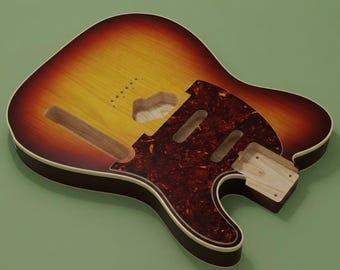 May include: An unfinished electric guitar body featuring a sunburst finish that transitions from a yellow center to a dark red edge. The body includes a tortoiseshell patterned pickguard, routed cavities for pickups and electronics, and a neck pocket.