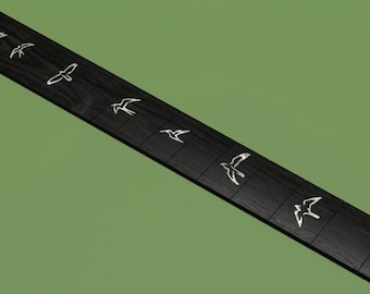 May include: A long, rectangular black guitar fretboard featuring a series of inlaid white bird silhouettes positioned along the center. The dark wood grain is visible across the surface, with each bird design appearing in a different flight pose.