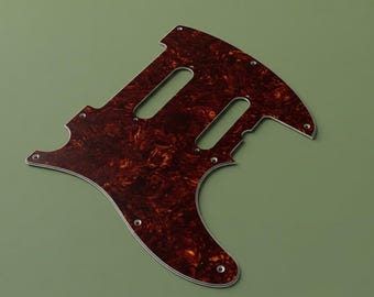 May include: A tortoise shell patterned guitar pickguard featuring a multi-layered design with two rectangular cutouts for pickups and several small circular screw holes positioned along the perimeter of the flat, contoured plastic component.