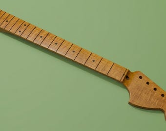 May include: A light brown wooden guitar neck featuring a fretboard with dark circular position markers and metal frets. The headstock includes six pre-drilled holes for tuning pegs, showcasing a natural wood grain finish throughout the entire piece.