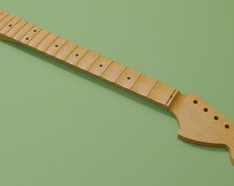 May include: A light brown wooden guitar neck featuring a smooth fretboard with dark circular fret markers and a headstock with six pre-drilled holes for tuning pegs. The neck has a natural wood grain finish and a standard elongated shape.