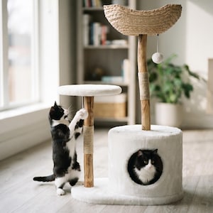May include: A cat tree featuring a white plush circular base with a matching enclosed hideaway, a white plush platform, and a woven basket top. Two wooden posts are wrapped with sisal rope, and a white pom-pom toy hangs from the basket.