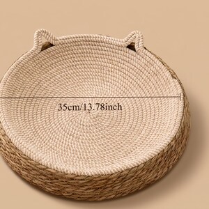 Pode incluir: Uma cama redonda para animais de estima&ccedil;&atilde;o com interior em corda bege enrolada e exterior em palha tran&ccedil;ada natural. A cama inclui dois pequenos detalhes elevados em forma de orelha na borda. Uma linha indica um di&acirc;metro de 35cm.