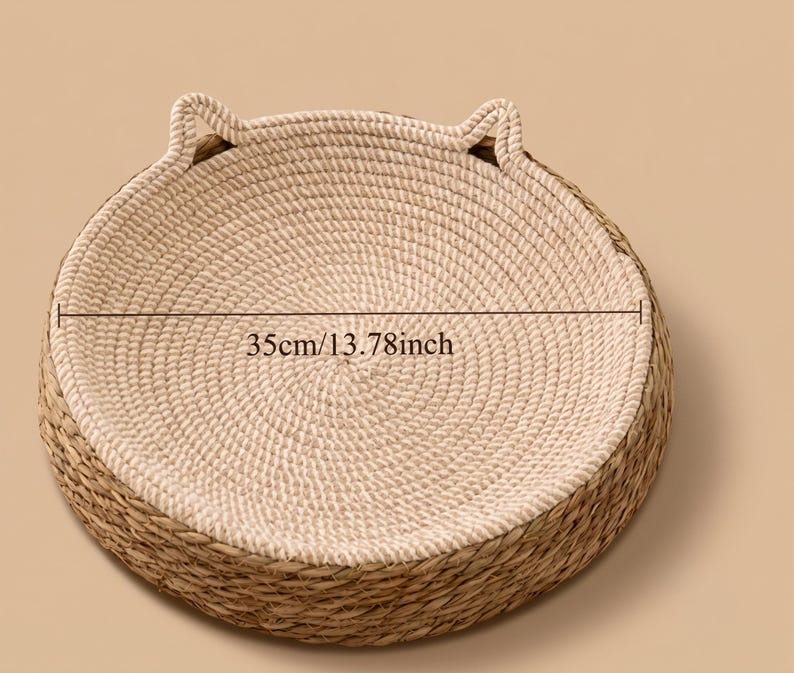 Pode incluir: Uma cama redonda para animais de estima&ccedil;&atilde;o com interior em corda bege enrolada e exterior em palha tran&ccedil;ada natural. A cama inclui dois pequenos detalhes elevados em forma de orelha na borda. Uma linha indica um di&acirc;metro de 35cm.