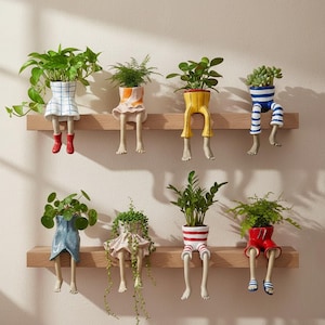 May include: Eight ceramic planters shaped like lower bodies with dangling legs, each holding a different green plant. The planters feature various colourful outfits including skirts, shorts, and trousers with patterns like stripes, checks, and solid colours.