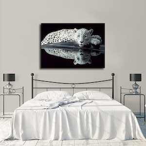 May include: A rectangular wall art print featuring a white leopard with black spots resting on a dark, reflective surface. The leopard is positioned horizontally against a solid black background, with its clear reflection visible directly below it.