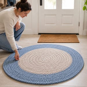 May include: A round, hand-crocheted rug featuring a large, solid beige center circle surrounded by a wide, solid blue border. The rug is constructed with a thick, textured yarn in a continuous spiral pattern, creating a flat, circular floor covering.