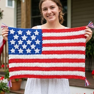 May include: A rectangular crochet wall hanging featuring the American flag design with a blue canton containing white stars and alternating red and white horizontal stripes, finished with small red, white, and blue tassels at each corner.