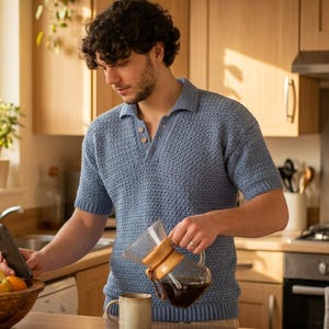 Peut inclure: Un polo bleu à manches courtes avec une texture tricotée, un col et deux boutons à l'encolure. Le vêtement est porté tout en tenant un smartphone et en versant du café depuis une carafe en verre dotée d'une poignée en cuir beige.
