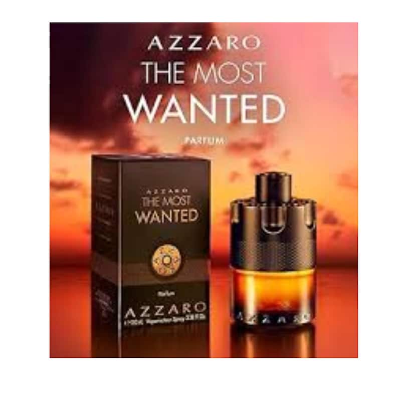 Op de afbeelding: Een fles Azzaro The Most Wanted Parfum naast de rechthoekige doos. De fles heeft een donkere, cilindrische dop met een textuurband en een heldere glazen voet met amberkleurige vloeistof. De doos is zwart met goudkleurige tekst en een embleem.