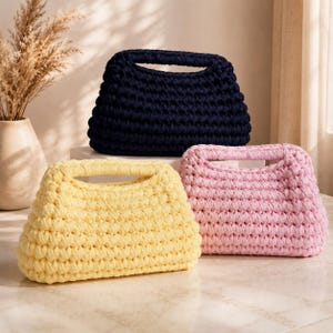 Peut inclure: Trois sacs à main en crochet faits à la main dans des couleurs unies. Un sac est bleu marine foncé, un est jaune pastel clair et un est rose bébé doux. Chaque sac présente un motif en maille épaisse et texturée avec une poignée intégrée.