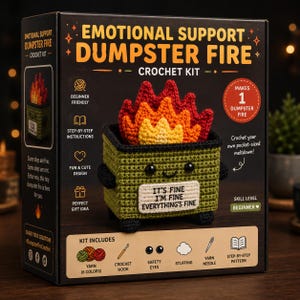 Op de afbeelding: Een zwarte doos voor een Emotional Support Dumpster Fire haakpakket met een groene afvalcontainer met zwarte ogen, een glimlachende mond en een wit bordje met de tekst IT'S FINE I'M FINE EVERYTHING'S FINE, bekroond met gehaakte rode en gele vlammen.