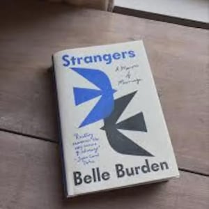 Puede incluir: Un libro de tapa dura titulado Strangers: A Memoir of Marriage de Belle Burden. La cubierta blanca presenta un gráfico de un pájaro azul y un gráfico de un pájaro negro. Hay una pequeña cita de estilo manuscrito impresa en la parte inferior izquierda.