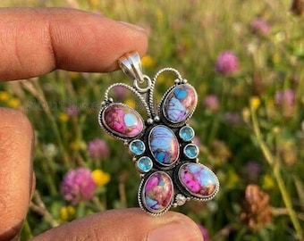 May include: A butterfly-shaped pendant crafted from sterling silver, featuring five oval-cut stones with marbled purple, blue, and pink patterns. The design is accented with four small, round, light blue faceted stones and a silver bail.