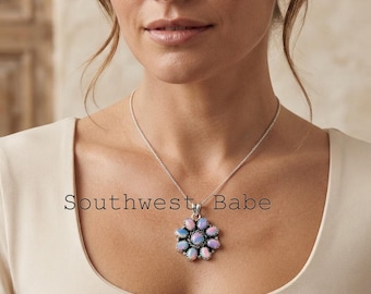 May include: A silver necklace featuring a flower-shaped pendant with iridescent oval stones arranged in a circular pattern. The text Southwest Babe is visible. The pendant hangs from a thin silver chain resting against a plain light-colored top.