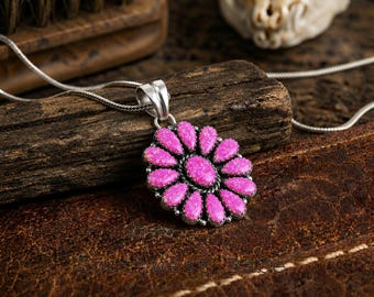 May include: A silver pendant necklace featuring a flower-shaped cluster of bright pink, speckled stones arranged in a radial pattern around a central oval stone. The pendant hangs from a thin silver chain, with the text Southwest Babe visible.