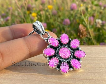 May include: A silver pendant shaped like a flower with a central circular pink stone surrounded by eight oval pink stones. The metal setting features a twisted rope texture around the center stone and a decorative bail at the top for a chain.