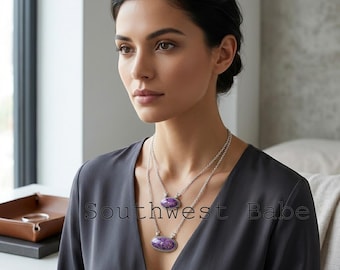 May include: A layered silver necklace featuring two oval purple stone pendants with textured metal settings. The jewelry is worn over a dark gray V-neck top. The text "Southwest Babe" is overlaid in the center of the image in a thin black font.