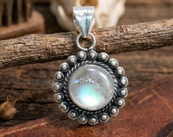 May include: A round silver pendant featuring a central iridescent moonstone cabochon surrounded by a twisted rope border and a ring of small silver spheres. The pendant has a smooth silver bail at the top and the text Southwest Babe is visible.