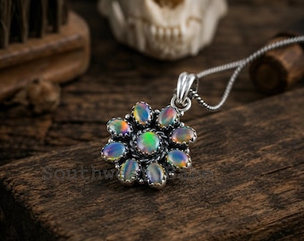 May include: A silver pendant necklace featuring a central oval opal surrounded by eight smaller oval opals in a floral arrangement. The stones display iridescent flashes of green, blue, and orange. The pendant hangs from a thin silver chain.