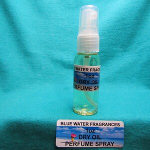 May include: A clear glass perfume spray bottle with a white cap and a blue and white label that reads "BLUE WATER FRAGRANCES 1oz DRY OIL PERFUME SPRAY". The bottle contains a light green liquid.
