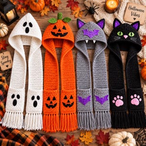 May include: Four crochet hooded scarves featuring Halloween themes. One white ghost, one orange pumpkin, one gray bat with purple accents, and one black cat with green eyes and pink paw prints. Each scarf has long fringe and deep pockets at the ends.