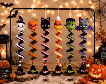 May include: Six hanging crochet Halloween ornaments featuring a ghost, pumpkin, black cat, candy corn, Frankenstein monster, and bat. Each figure sits atop a colorful spiral tail ending in a small black witch hat base with a yellow buckle.