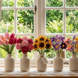 May include: Five ceramic vases containing handmade crochet flowers, including pink tulips, red roses, yellow sunflowers, purple daisies, and multicolored bell-shaped flowers. A small tag labeled Handmade Crochet is tied to the sunflower vase.