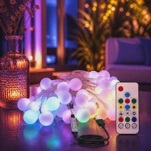 May include: A string of spherical LED lights with a translucent white finish, connected by a clear wire to a USB plug and a small controller. A rectangular remote control with multiple colored buttons and icons is positioned next to the lights.