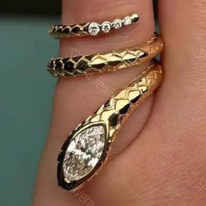 May include: A gold snake-shaped wrap ring featuring a textured scale pattern along the band, a marquise-cut white gemstone set in the head, and a row of four small round white gemstones embedded along the tail end of the coiled design.