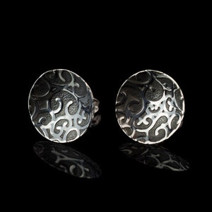 Può includere: Un paio di orecchini d'argento con un motivo nero, intricato e a spirale.