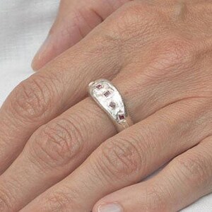 May include: A silver ring with a curved band and five small, square-shaped, pink gemstones.