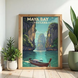 May include: A framed travel poster featuring a stylised illustration of Maya Bay, Thailand. The artwork depicts a long-tail boat on turquoise water surrounded by towering limestone cliffs. The text 'MAYA BAY THAILAND' is printed at the top.
