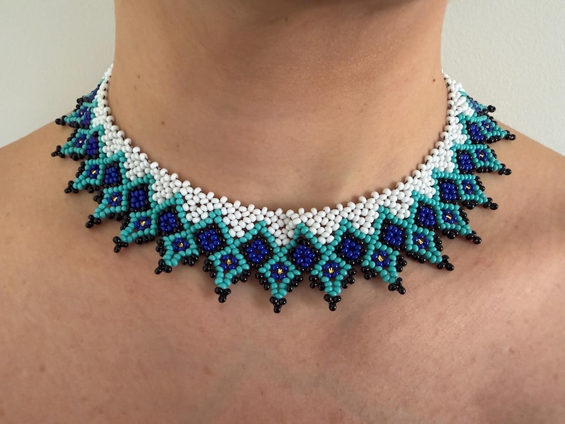 Beaded collar necklace in turquoise, blue, white and black with a scalloped diamond pattern, worn around the neck