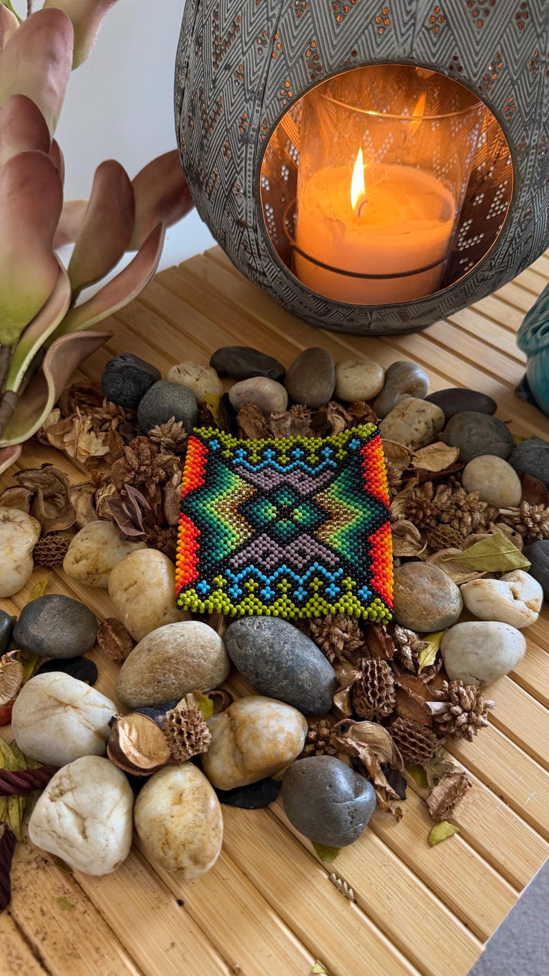 Noke Koî beaded bracelet with a vivid green and amber geometric diamond pattern, photographed on river stones