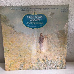 May include: A vintage vinyl record album cover featuring a painting of a couple in a field of flowers. The album is titled "Geza Anda plays and conducts Mozart Two Favorite Concertos No. 21 in C / No. 20 in D Minor Vienna Symphony Orchestra" and has the RCA Red Seal logo.