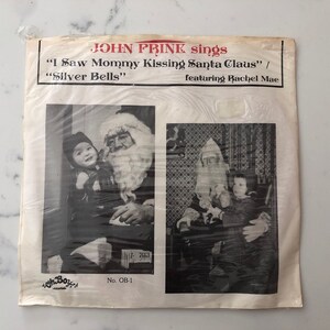 May include: Vintage vinyl record featuring John Prine singing "I Saw Mommy Kissing Santa Claus" and "Silver Bells." The black and white cover shows Santa Claus with a child. The record is in a plastic sleeve.