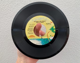 May include: Black vinyl record with a yellow label. The label has the text "Island" and "He Was A Big Freak" by Betty Davis. The record is labeled "IS 024-B" and has a playing time of 4:06.