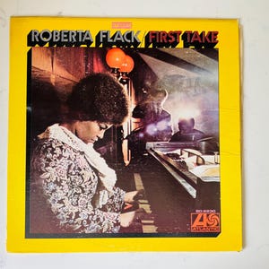 May include: Album cover for Roberta Flack's "First Take." The cover features a photo of Roberta Flack playing a piano, with the album title in bold text. The album has a yellow border and the Atlantic Records logo.