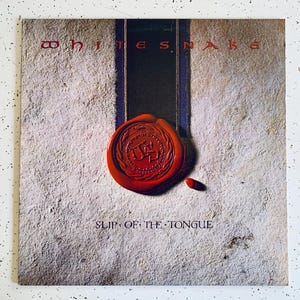 May include: A vintage vinyl record album cover for Whitesnake's album "Slip of the Tongue". The cover features a red wax seal with a snake design and the band's name in white text.
