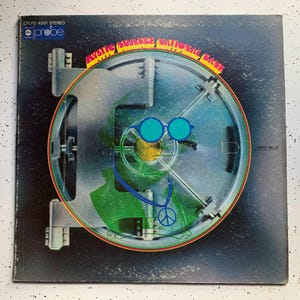May include: Vintage vinyl record album cover featuring a stylized bank vault door with a face created from the vault's components. The face has blue sunglasses and a peace sign. The album title is "Mystic Number National Bank."